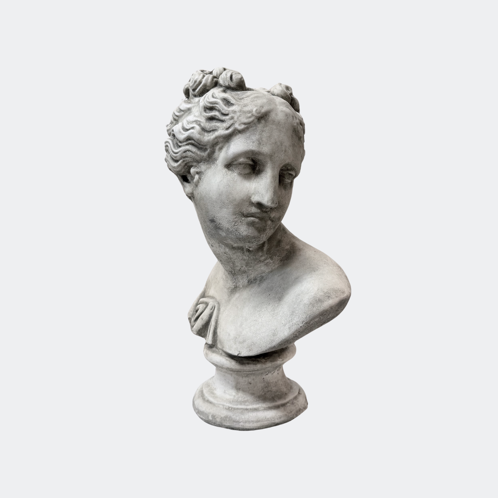 Classical female bust in aged cast stone, three-quarter profile with pinned wavy hair, on turned pedestal base