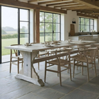 Dining room with a long wooden table and chairs, large windows, and a view of greenery outside.